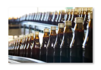 Reihe von Flaschen mit dunklem Getränk auf einem Förderband.