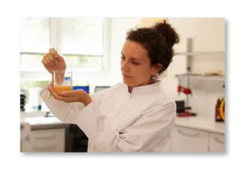 Eine Wissenschaftlerin in einem Labor hält ein Reagenzglas mit orangefarbener Flüssigkeit.