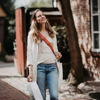 Junge Frau mit Einkaufstüten geht lächelnd auf einem gepflasterten Weg.