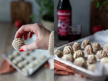 Eine Hand hält eine süße Kugel mit Zuckerguss, im Hintergrund weitere Kugeln auf einem Blech.