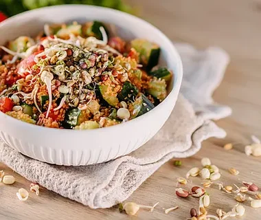 Schüssel mit Quinoa-Salat, Gemüse und Sprossen auf einem Tisch.