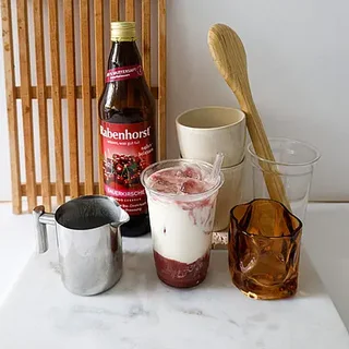 Verschiedene Gläser, ein Löffel und eine Flasche Kirschsaft auf einem Marmoruntergrund.