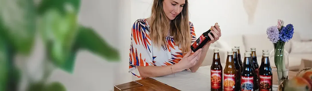 Eine Frau betrachtet eine Flasche Getränk, während mehrere Flaschen auf einem Tisch stehen.